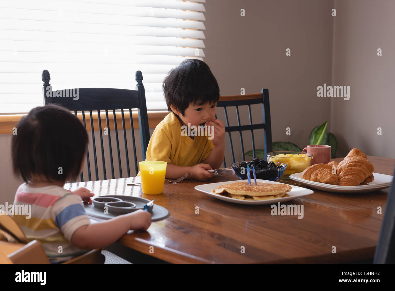 Kids having breakfast while sitting at dining table in kitchen Stock Photo