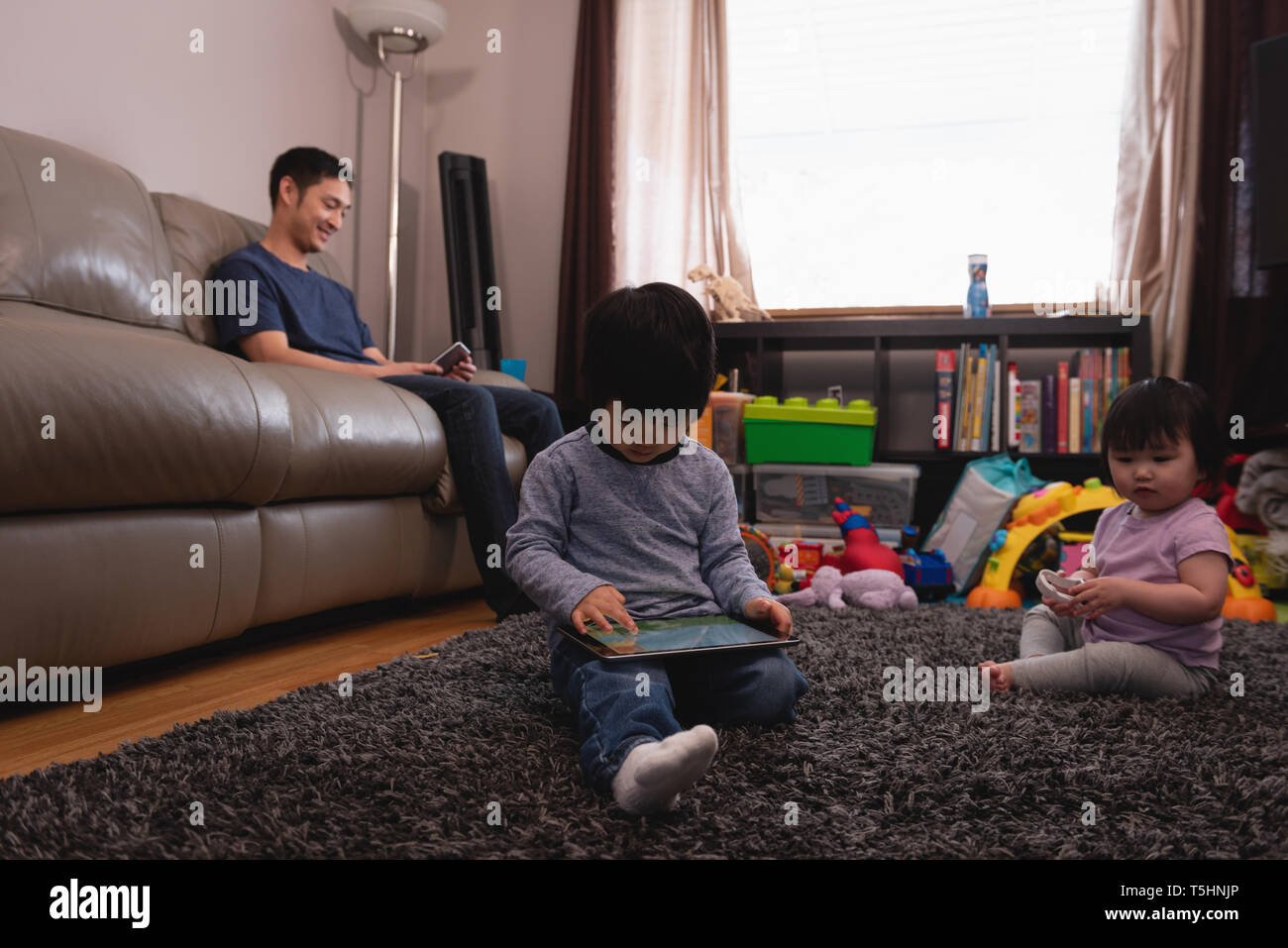 Father using mobile phone while kids playing at home Stock Photo