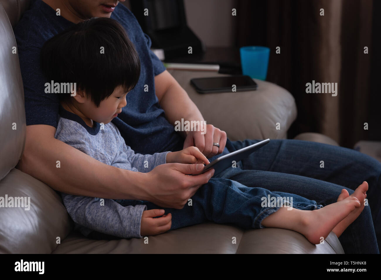 Father and son using digital tablet while sitting on sofa Stock Photo
