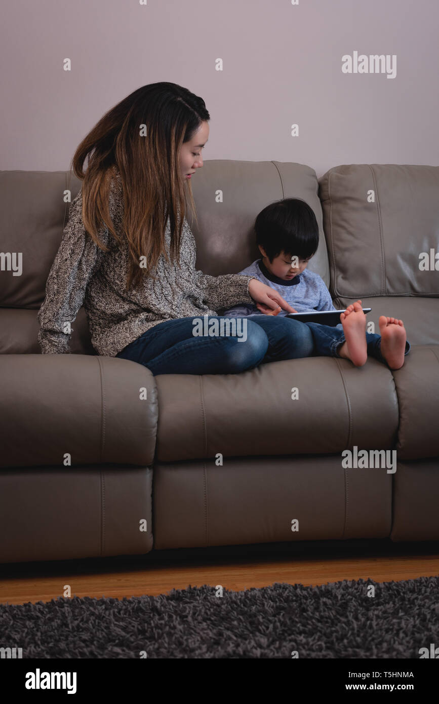 Mother and son using digital tablet while sitting on sofa at home Stock Photo