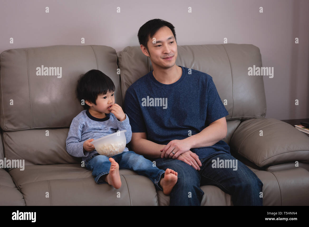 Father and son sitting on sofa at home Stock Photo