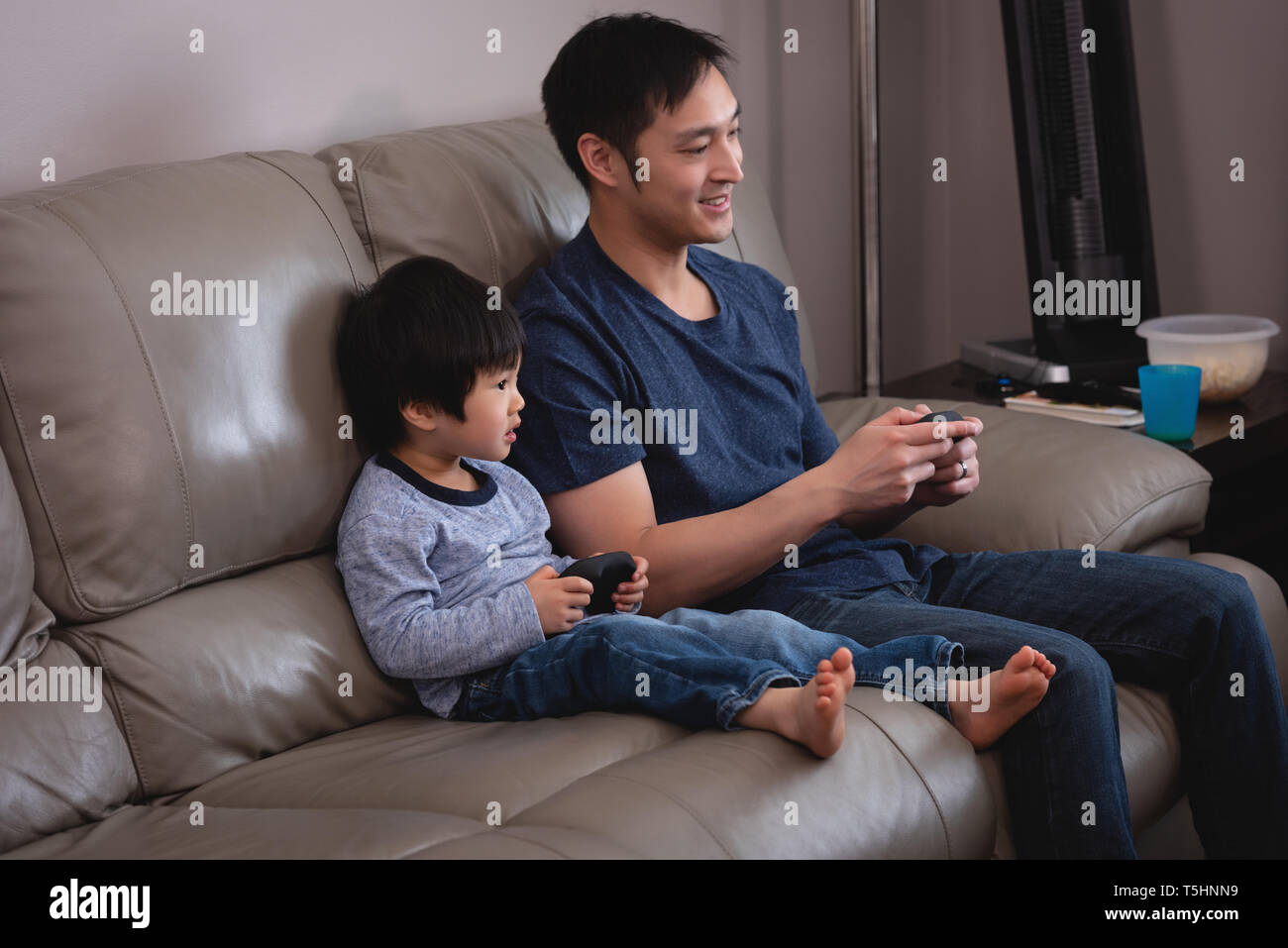 Father and son playing together video game while sitting on sofa at home Stock Photo