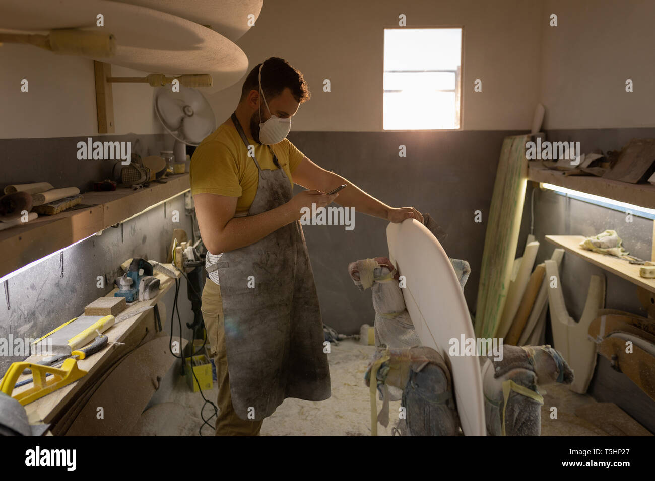 Man using mobile phone while cleaning surfboard in a workshop Stock Photo