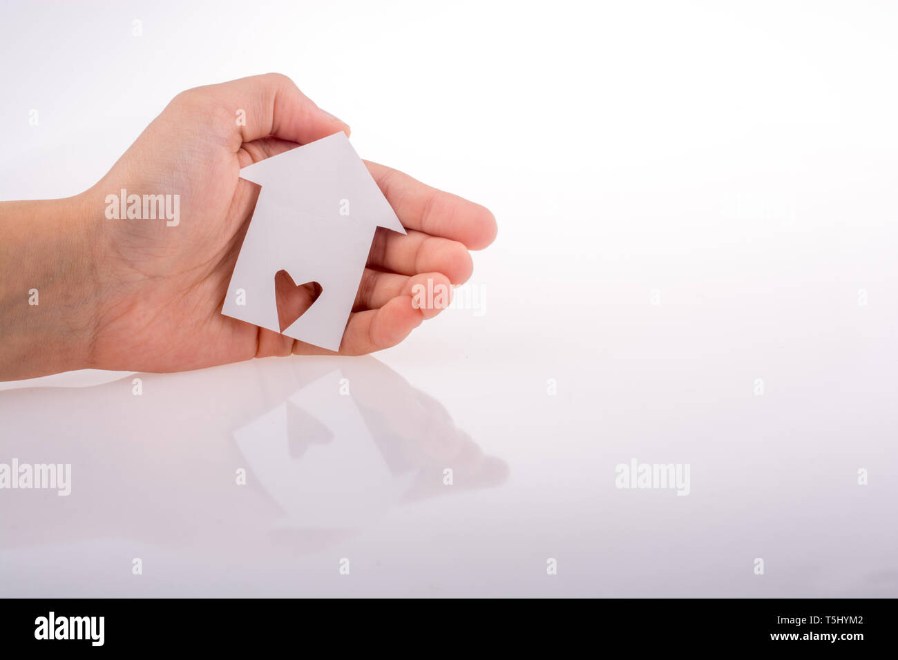 Hand holding a paper house with a heart carved in it on a white ...