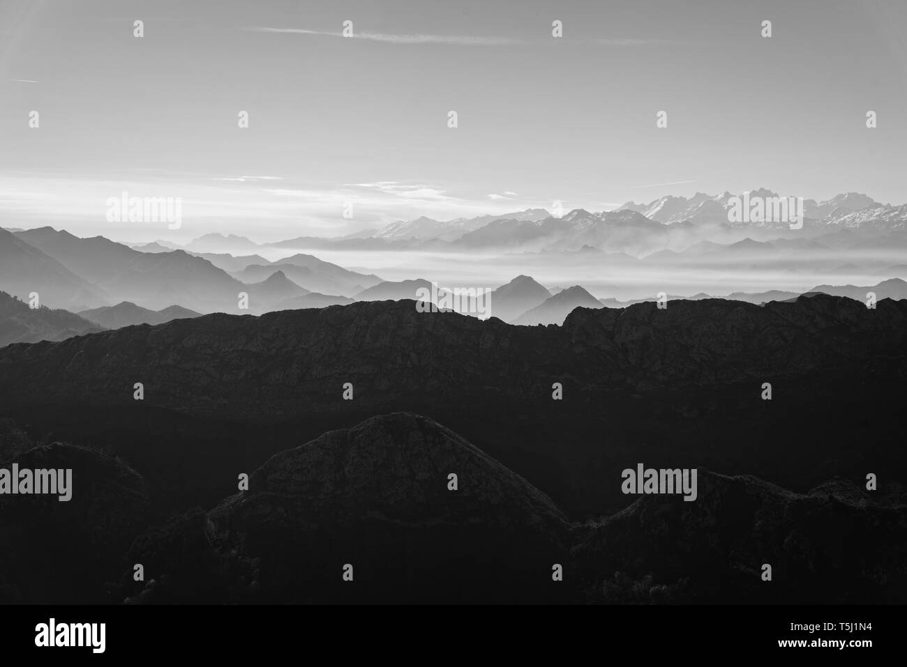 Scenic view of silhouettes of mountains in the morning mist with snowcapped mountains on background. Picos de Europa, Asturias, Spain Stock Photo