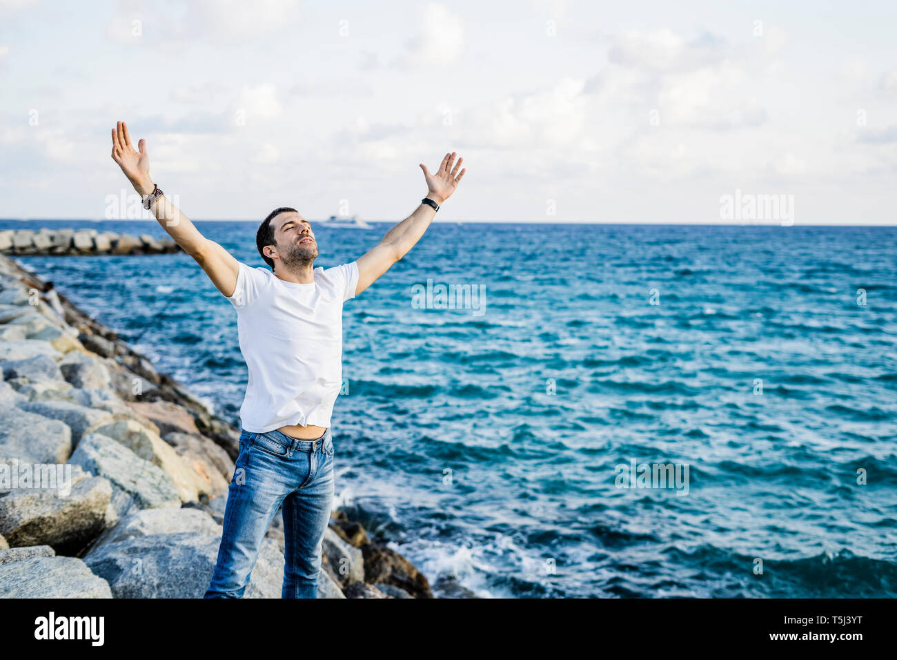 Man with raised arms and eyes closed standing in front of the sea Stock Photo