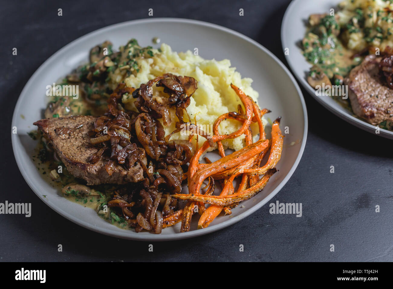 Beef sirloin steak with mushroom-mustard sauce, mashed potatoes, braised onions and carrot strips Stock Photo