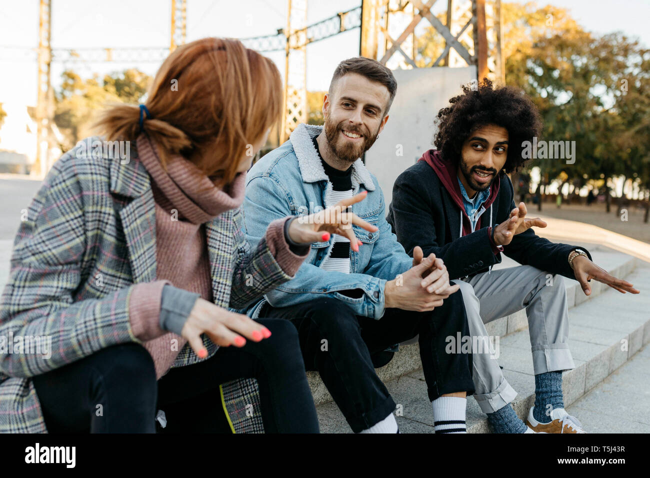 Three happy friends sitting outdoors alking Stock Photo
