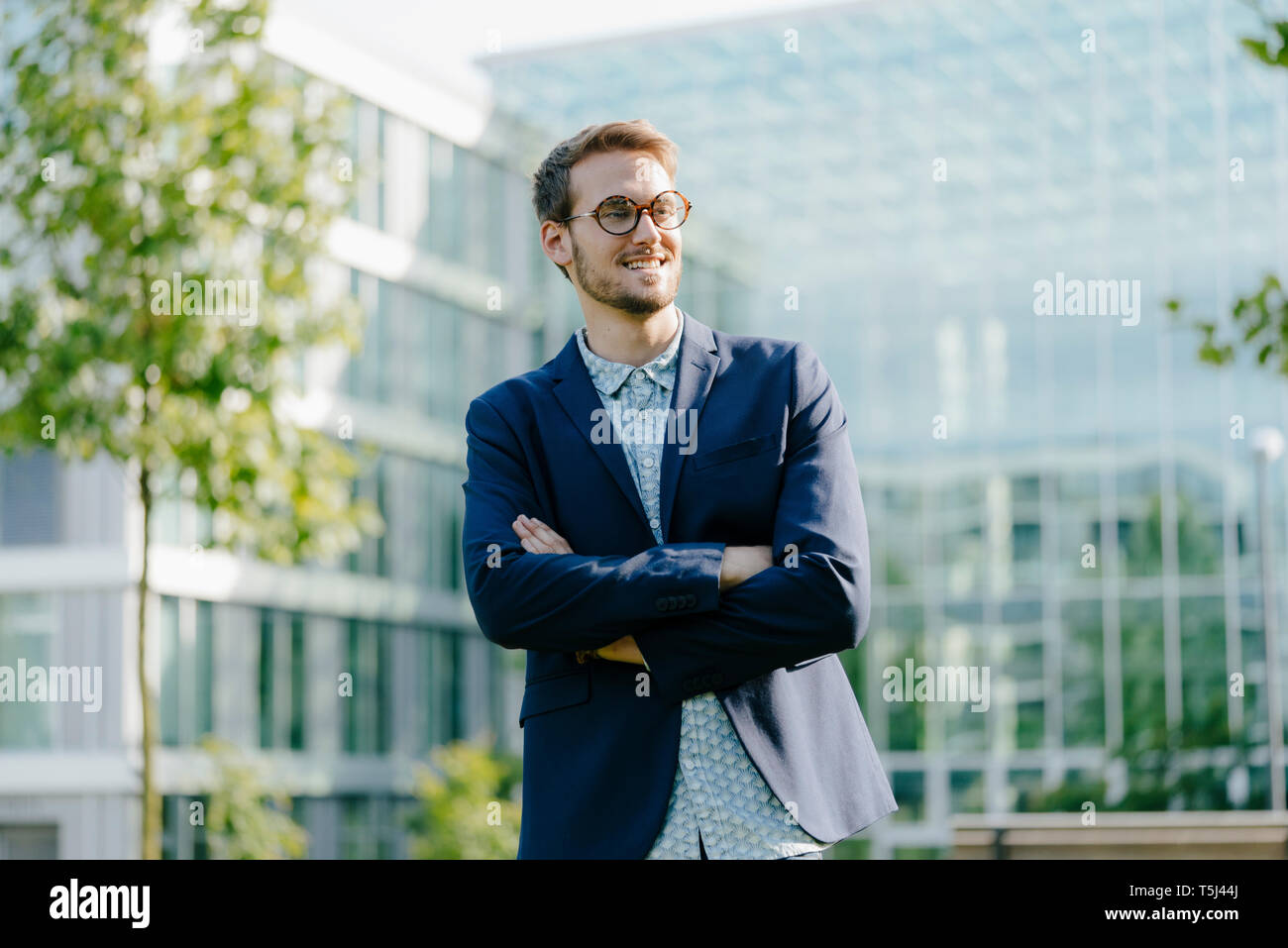 Young businessman standing in front of modern office building, with ...