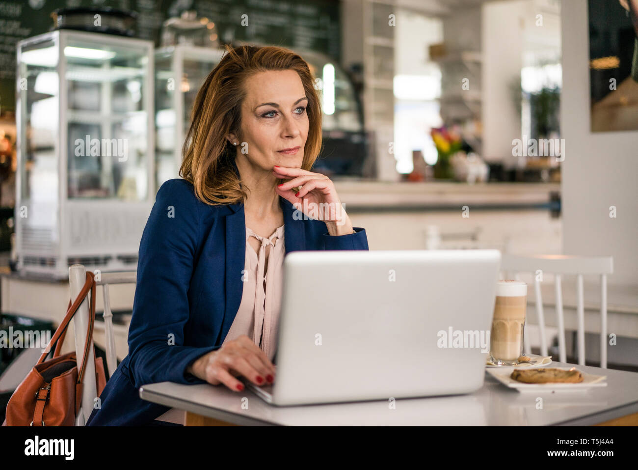 Businesswoman sitting in coffee shop, having lunch, working on laptop Stock Photo