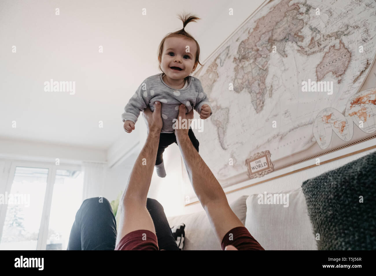 Happy baby girl being lifted up by her father in living room at home Stock Photo