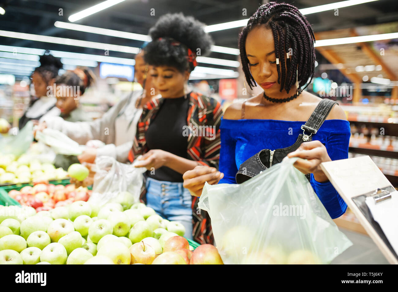 Group of five african womans picking up apples in plastic bags at