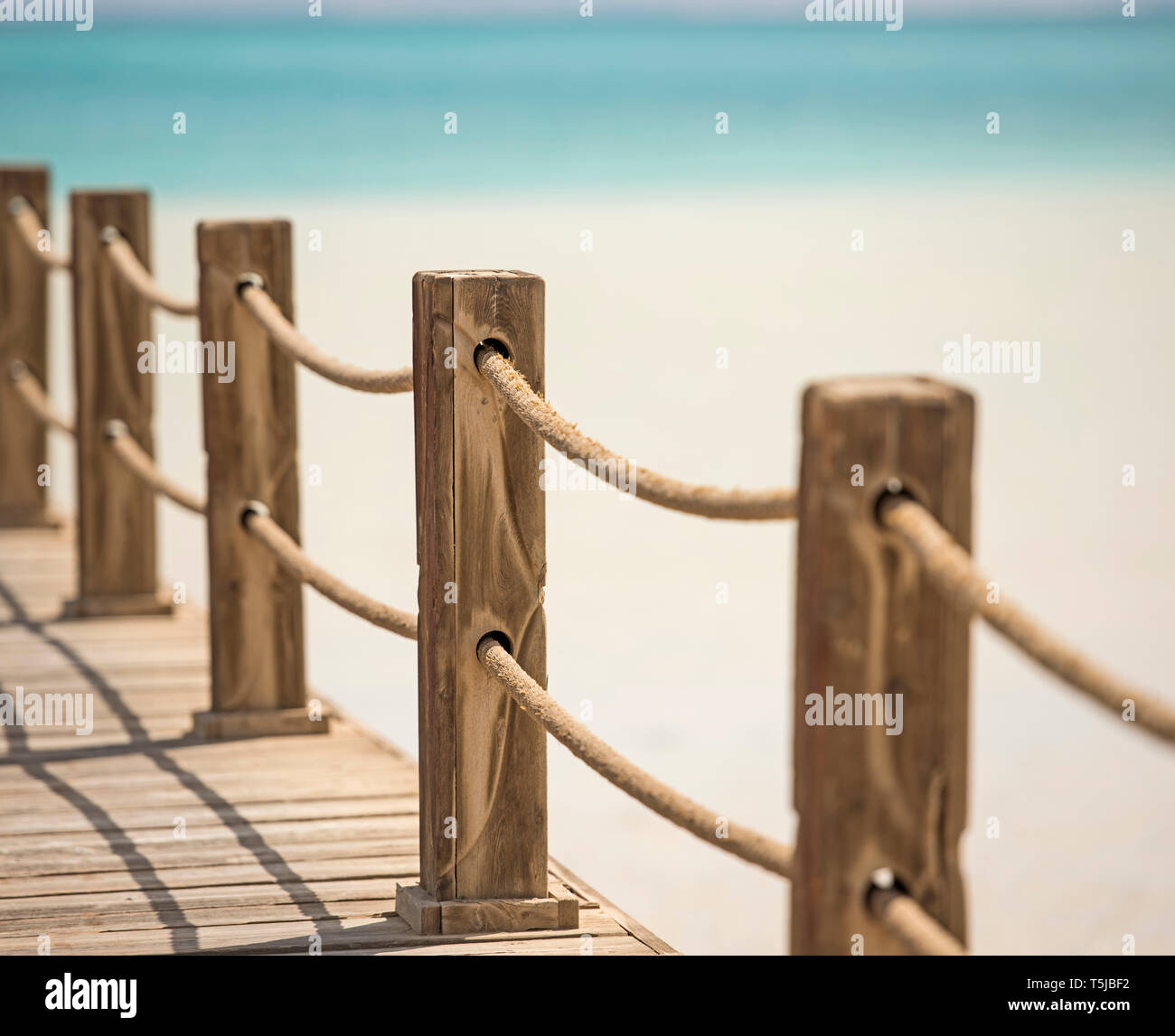 Wooden posts and rope railings on jetty over tropical sea with lagoon