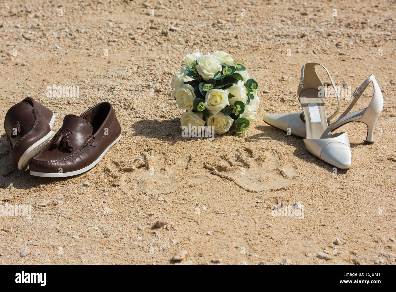 Bride and grooms shoes and handprints on beach in sand with wedding