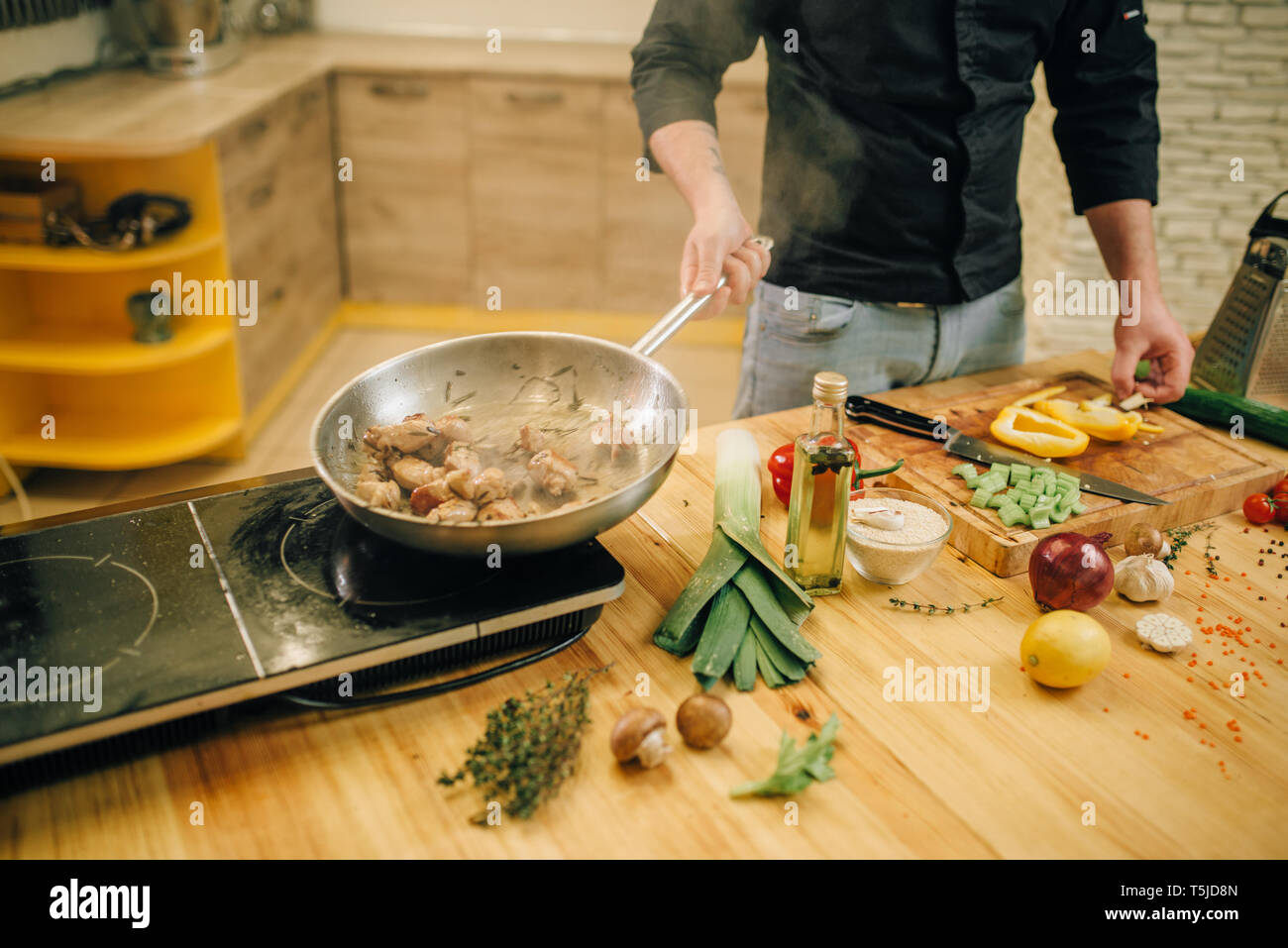 Male chef cooking meat with vetables into the frying pan on the kitchen ...