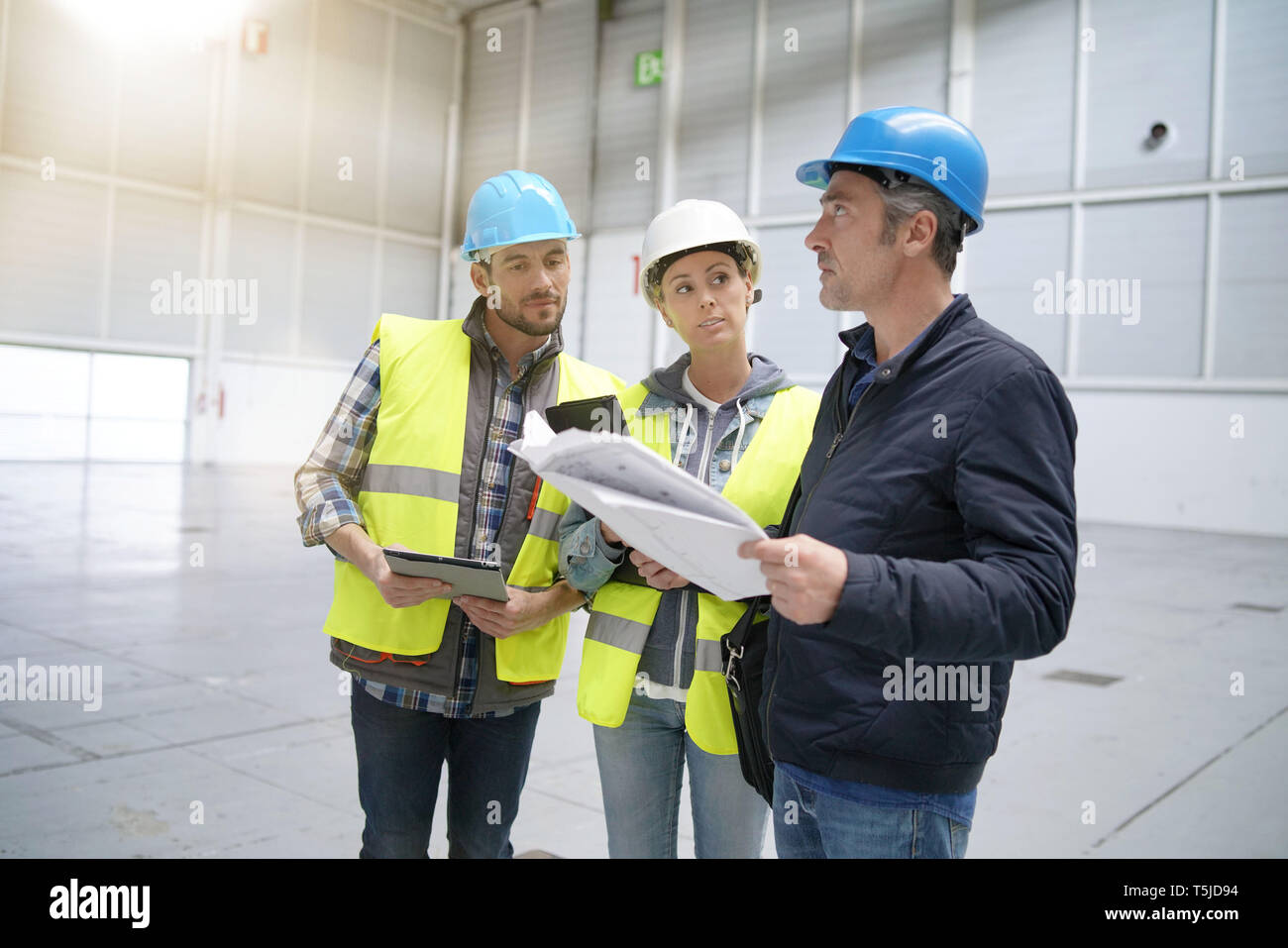Team of construction workers talking in empty warehouse Stock Photo