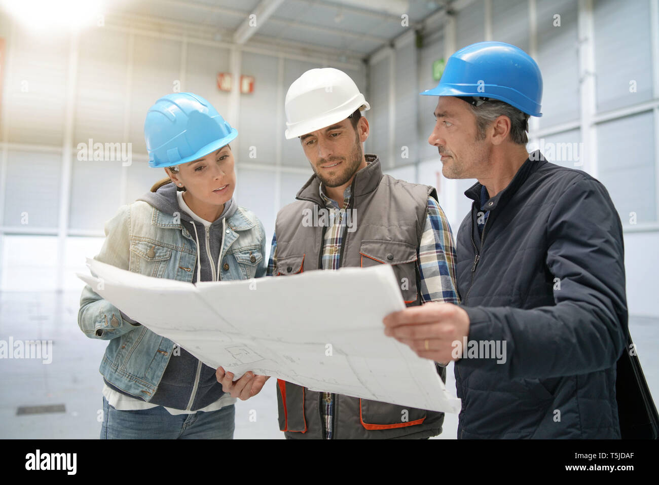 Team of construction workers talking in empty warehouse Stock Photo