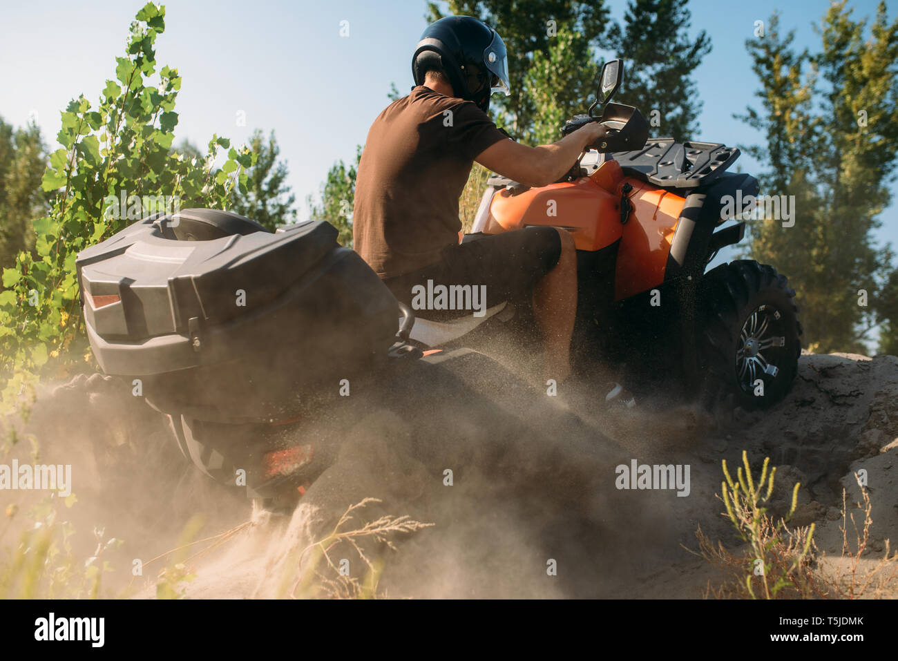 Atv rider climbing the sand mountain in quarry, back view, dust clouds
