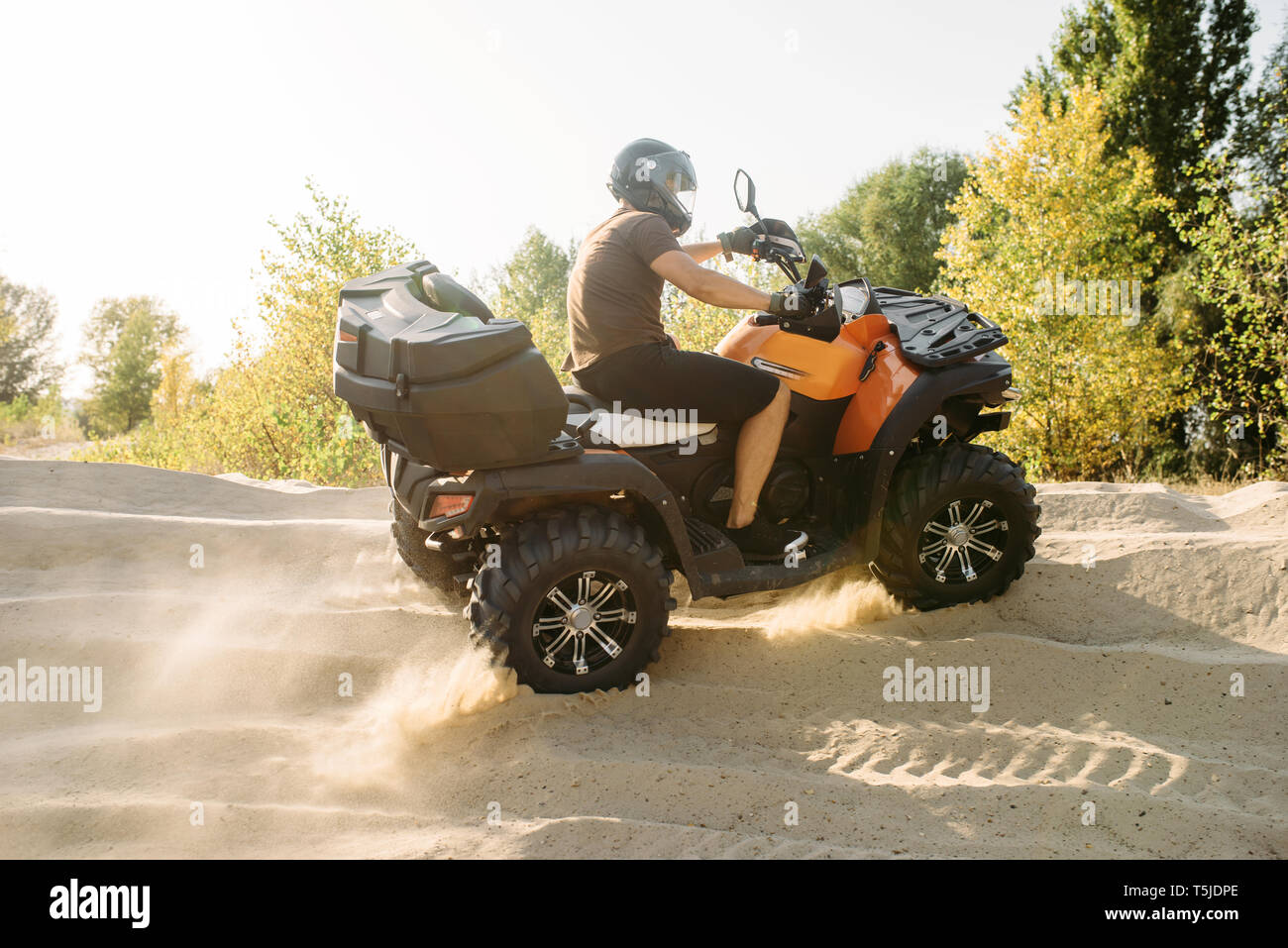 Atv riding in sand quarry, dust clouds. Male driver in helmet on quad