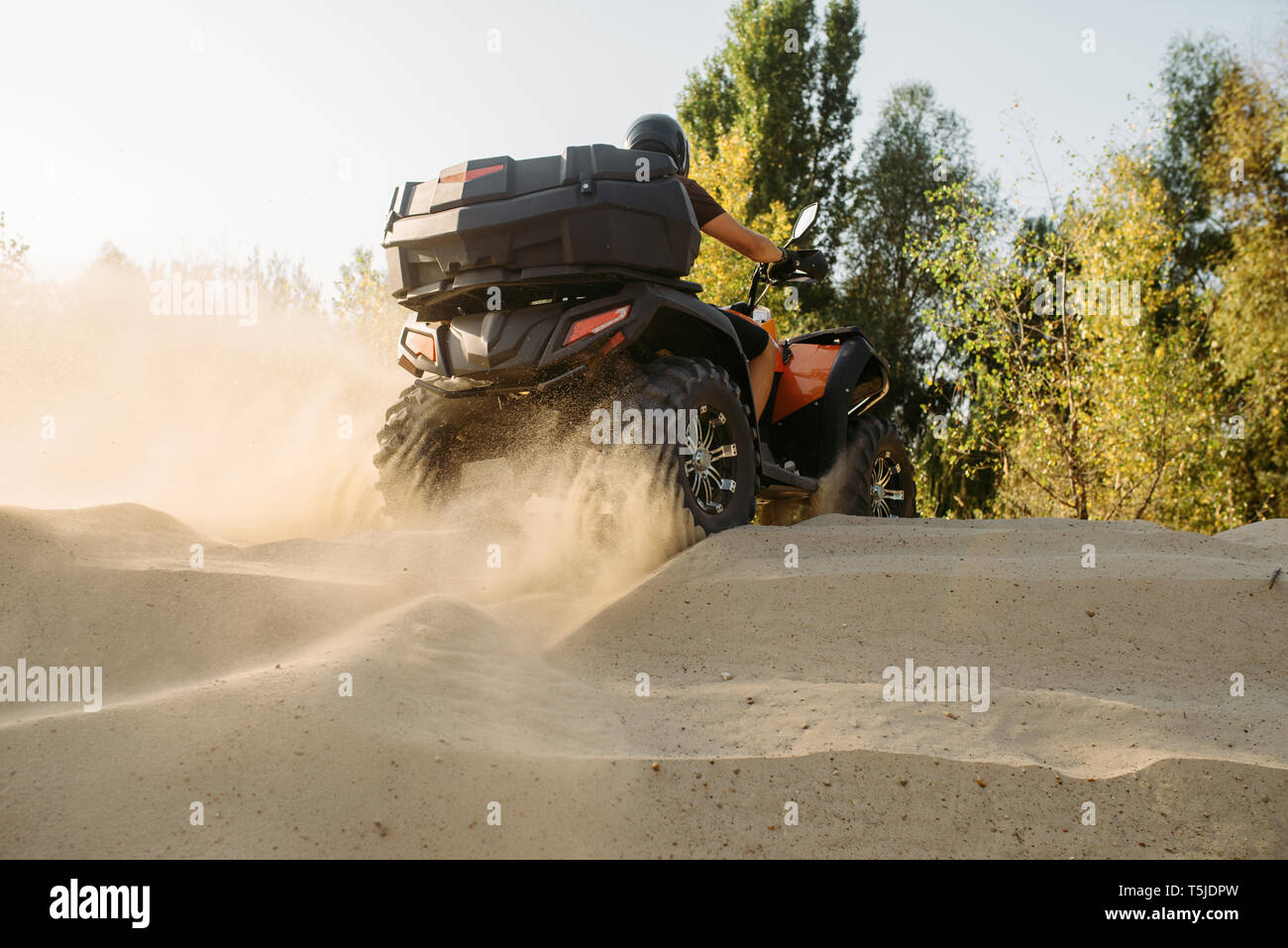 Atv riding in sand quarry, dust clouds. Male driver in helmet on quad