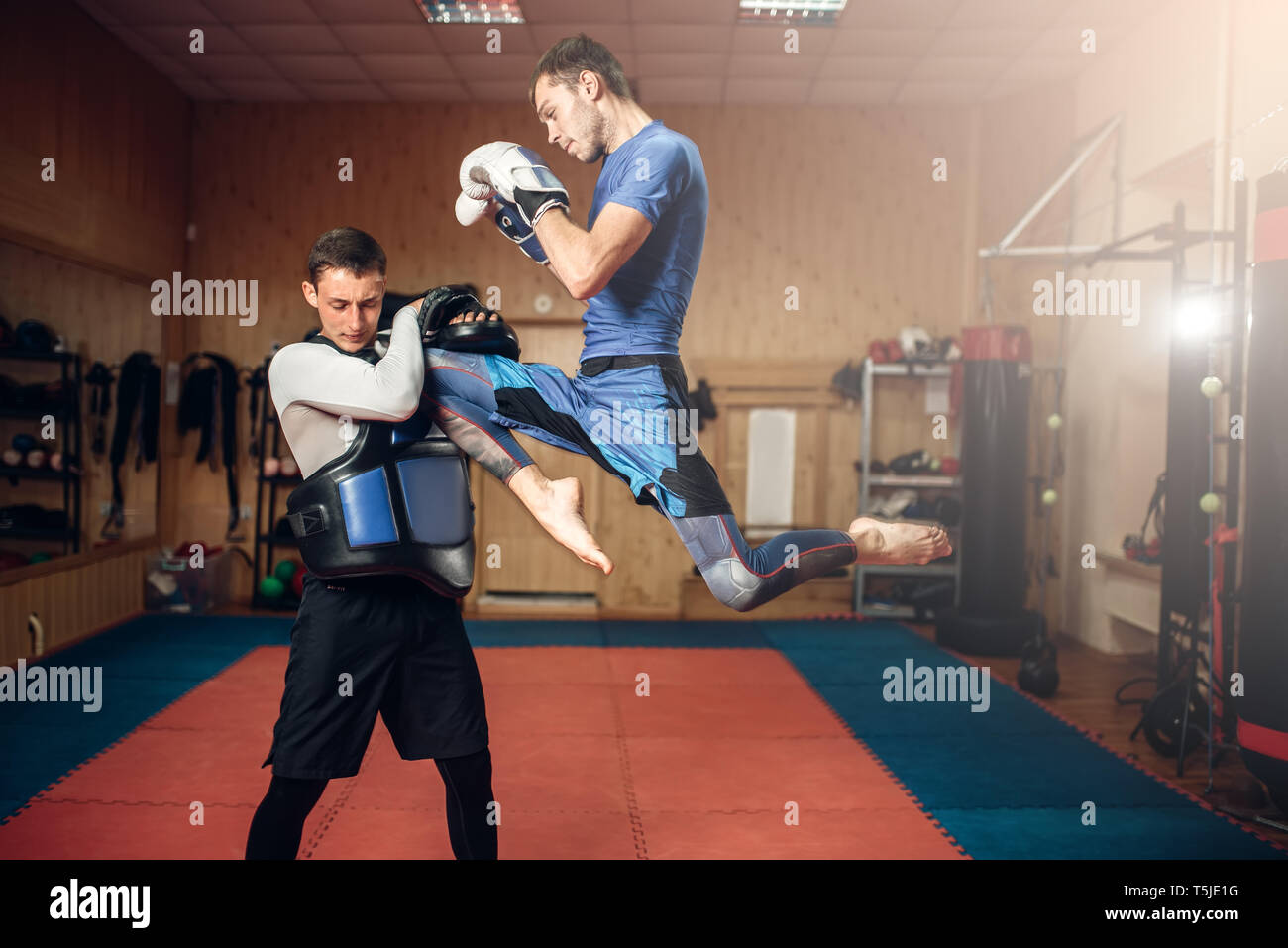 Male kickboxer doing kick in jump, practicing with a personal trainer, workout in gym. Boxer on