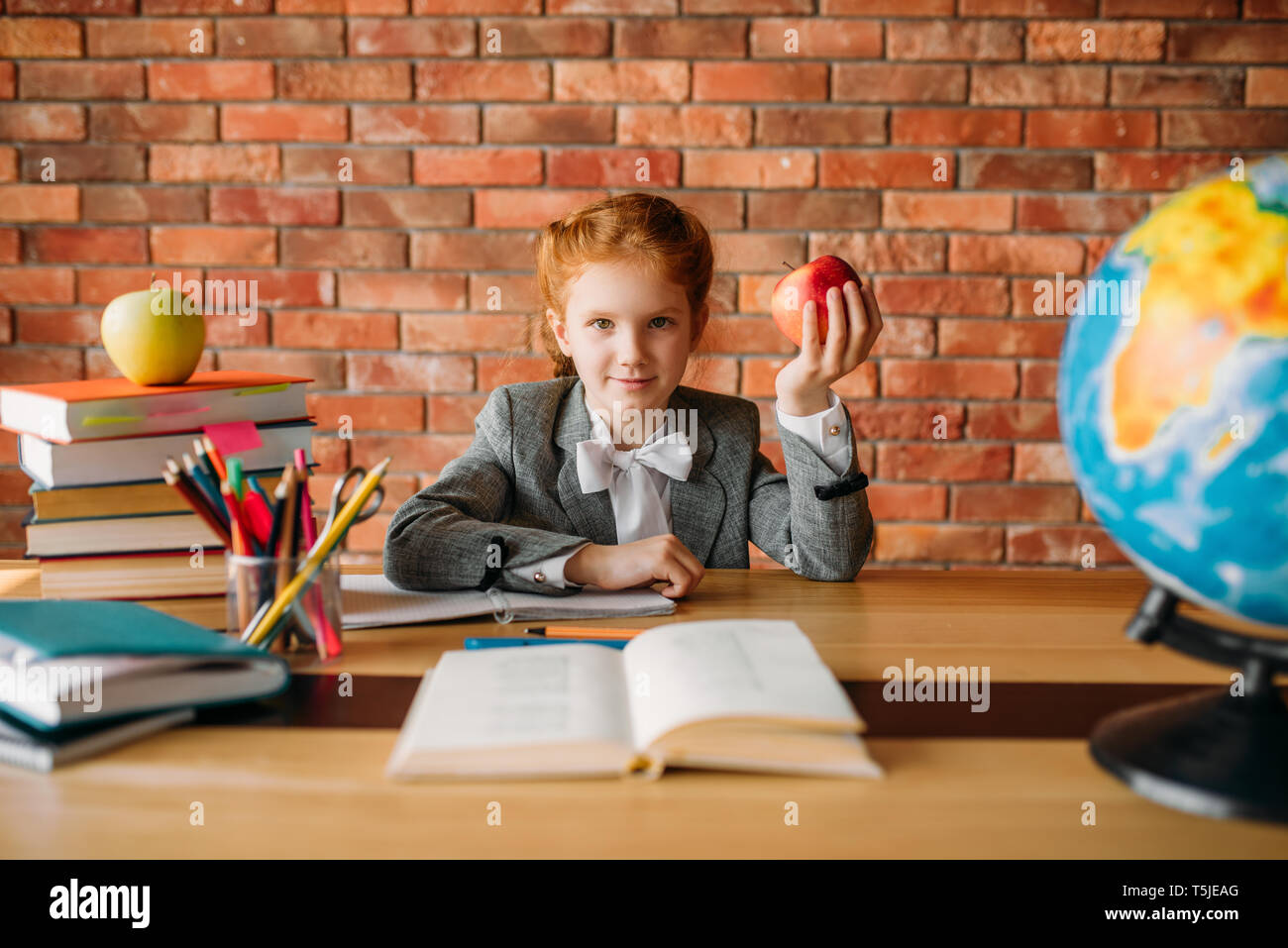 Funny schoolgirl with apple sitting at the table in classroom. Female ...