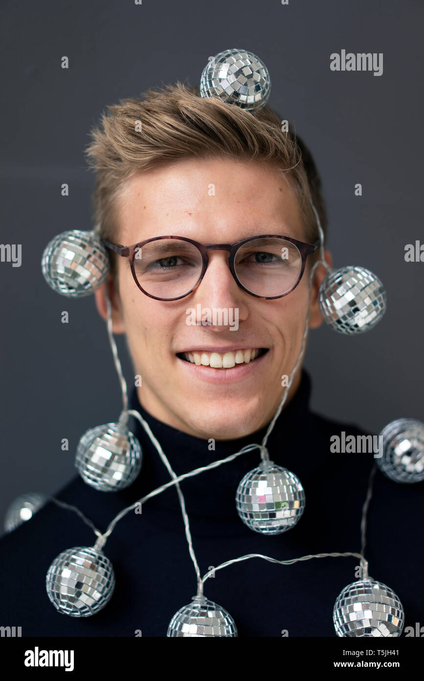 Portrait of smiling young man wearing mirror ball fairy lights Stock