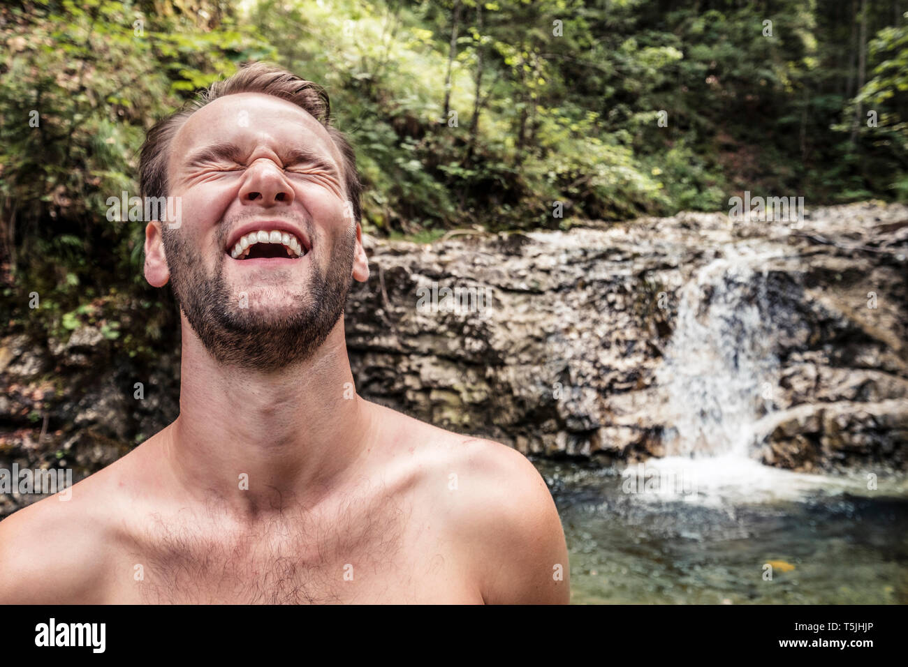 junger Mann lacht ausgelassen in einem Wildbach in den bayrischen Voralpen, Walchensee, Oberbayern, Deutschland. Stock Photo