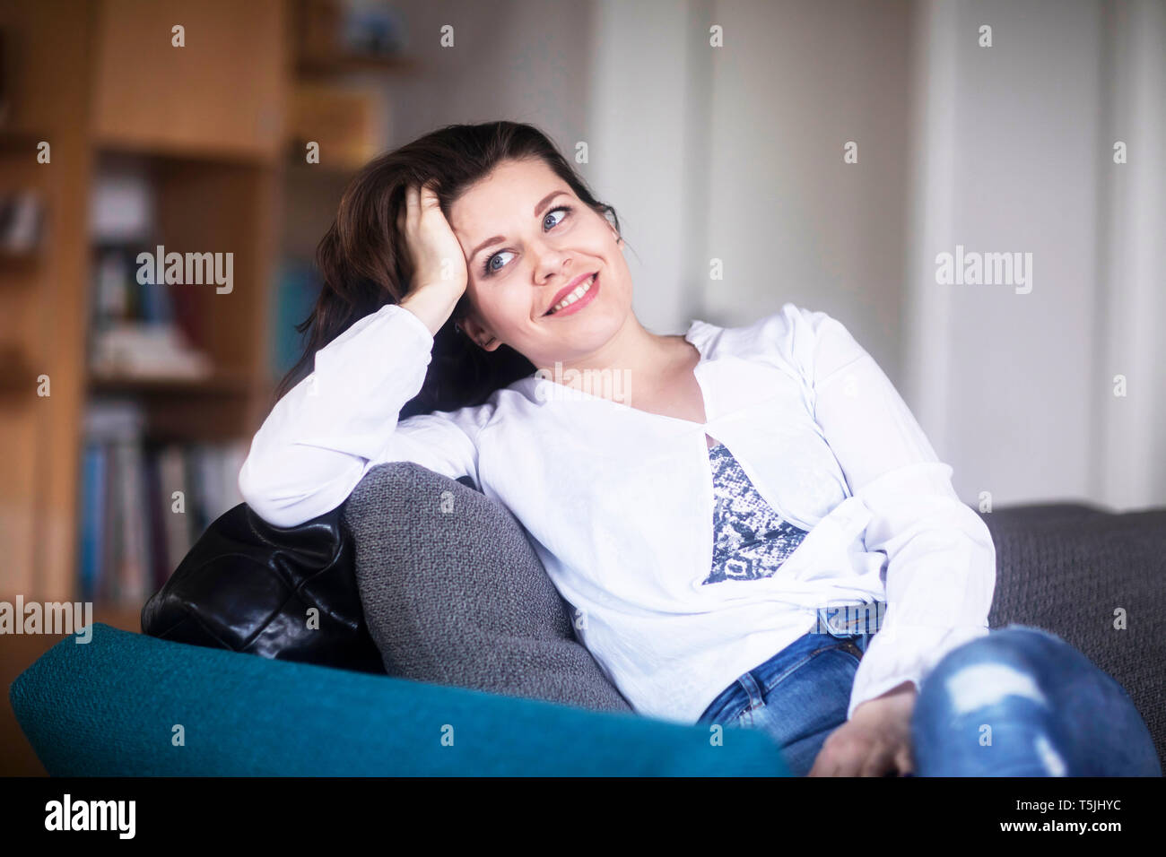 Portrait of smiling young woman sitting on couch at home relaxing Stock ...
