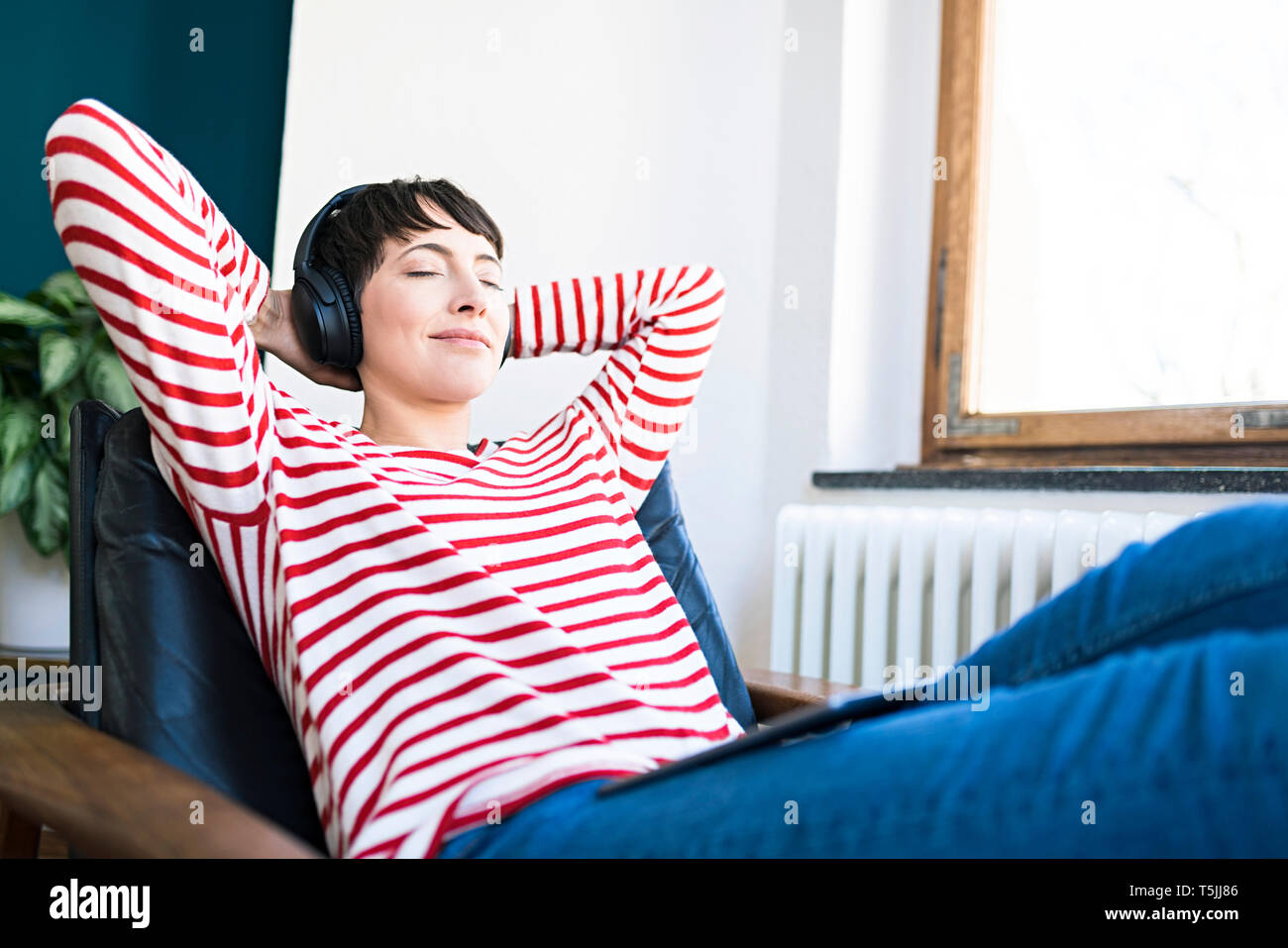 Short-haired woman with headphones relaxing in lounge chair Stock Photo