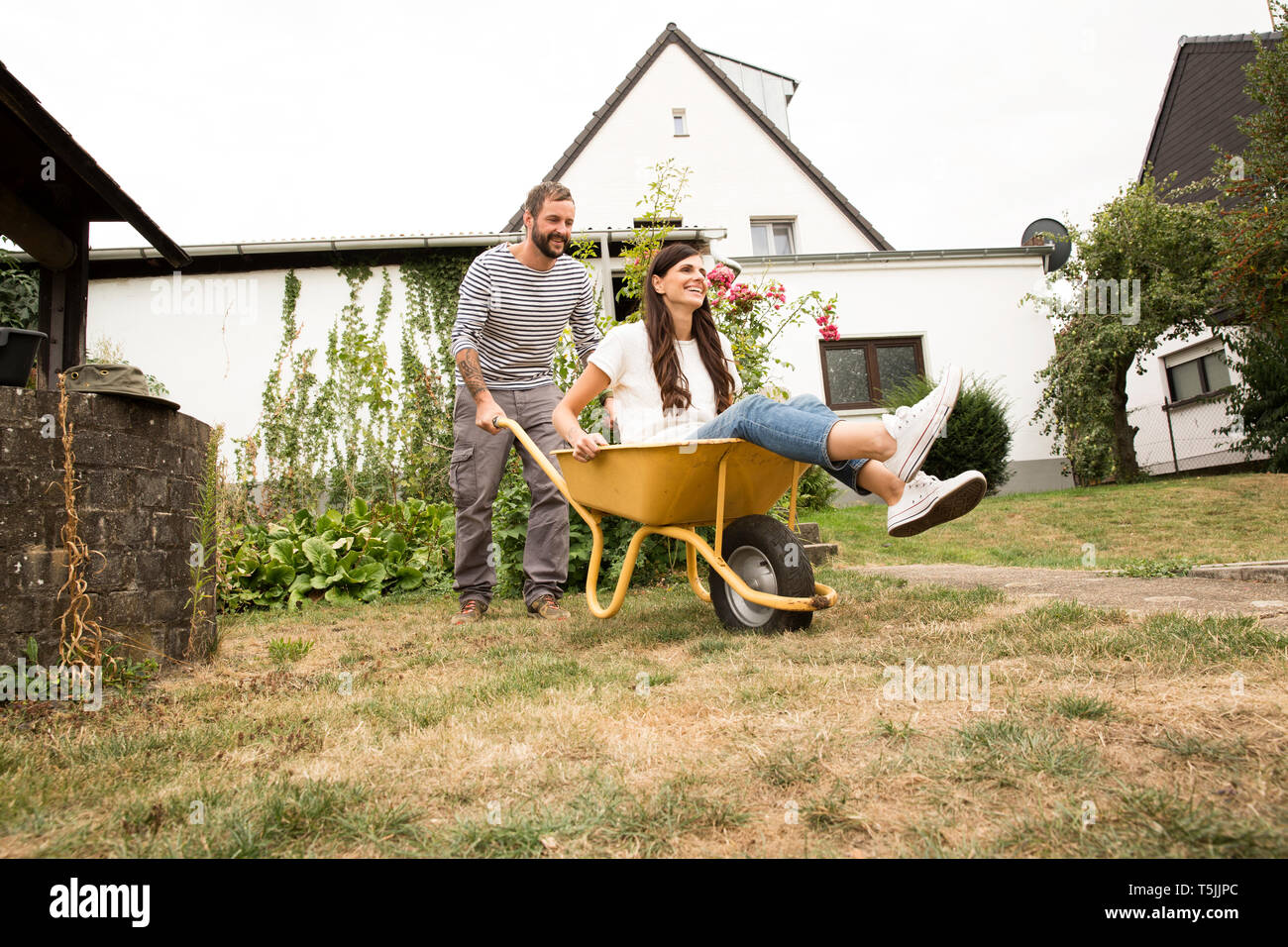 Playful man pushing woman sitting in wheelbarrow in garden Stock Photo ...