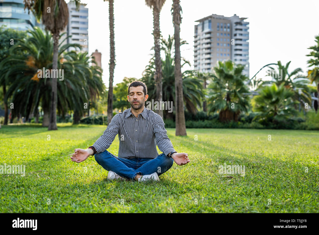 Man sitting on meadow in city park doing yoga exercise Stock Photo