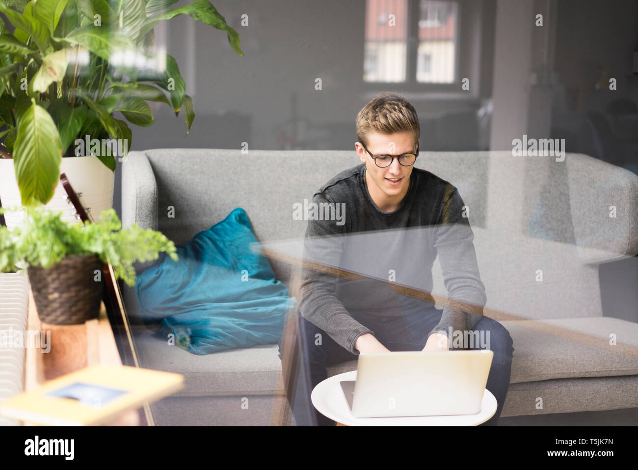 Young man sitting on couch using laptop Stock Photo