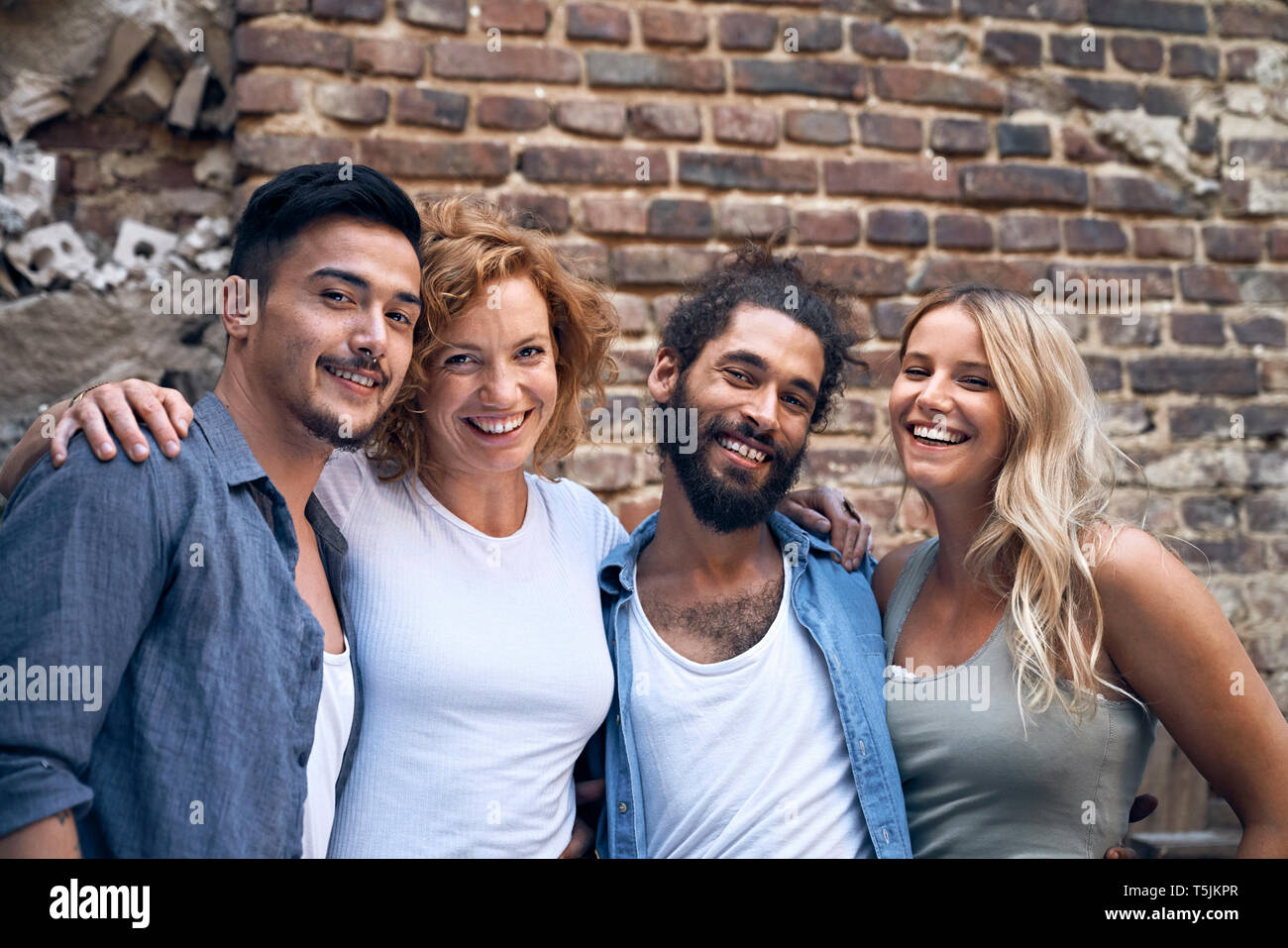Four friends standing in front of brick wall, with arms around Stock ...