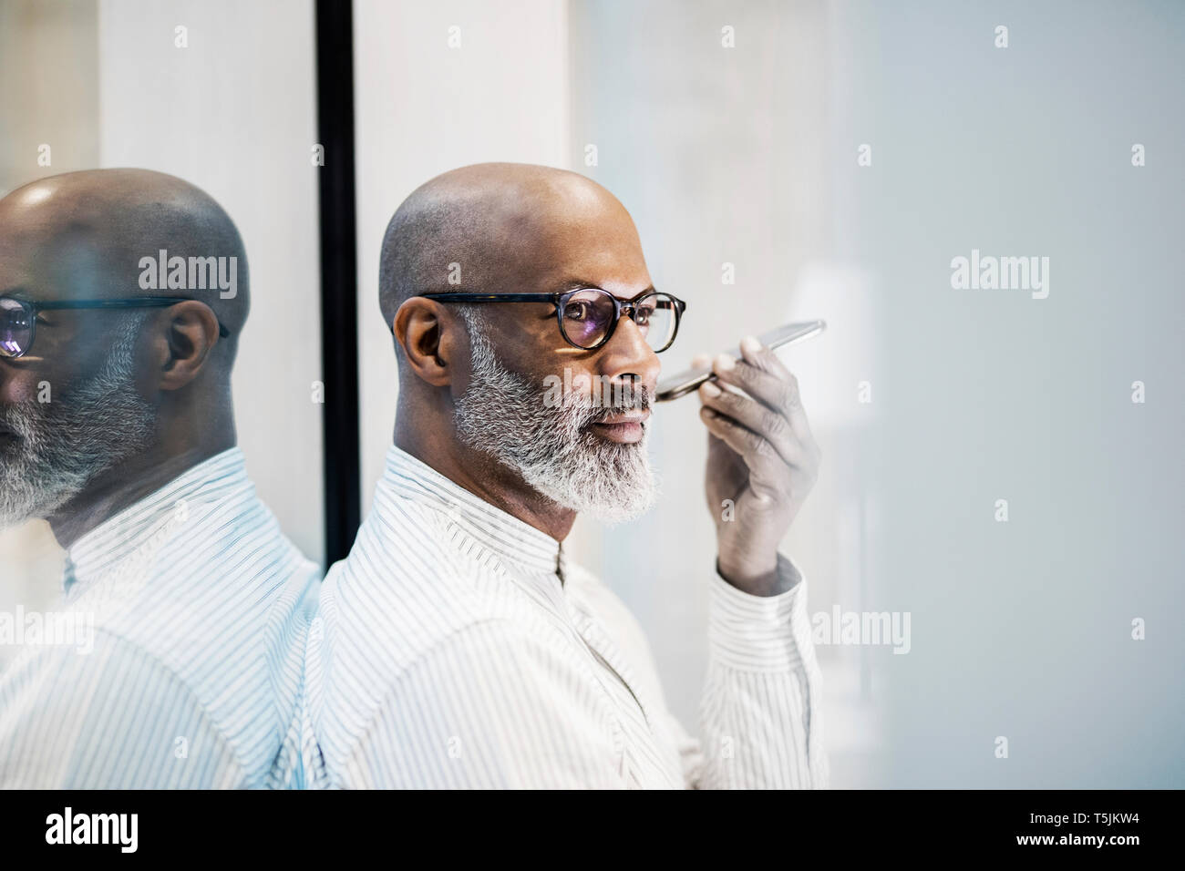 Portrait of bald mature businessman with grey beard using smartphone Stock Photo