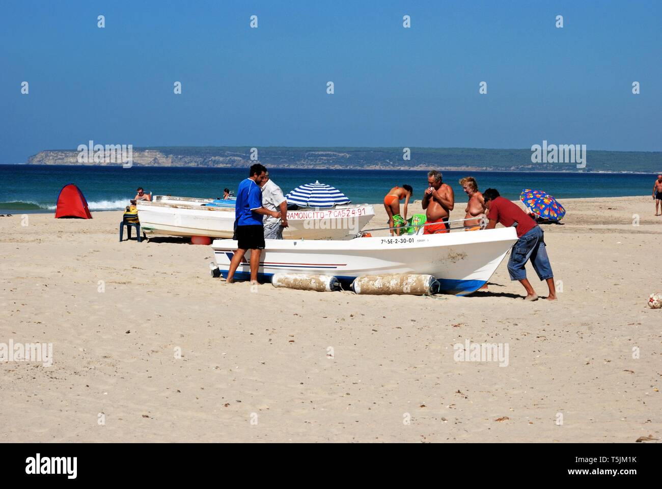 Wooden fishing boat on the beach with tourists enjoying the setting, Zahara de los Atunes, Cadiz Province, Spain. Stock Photo