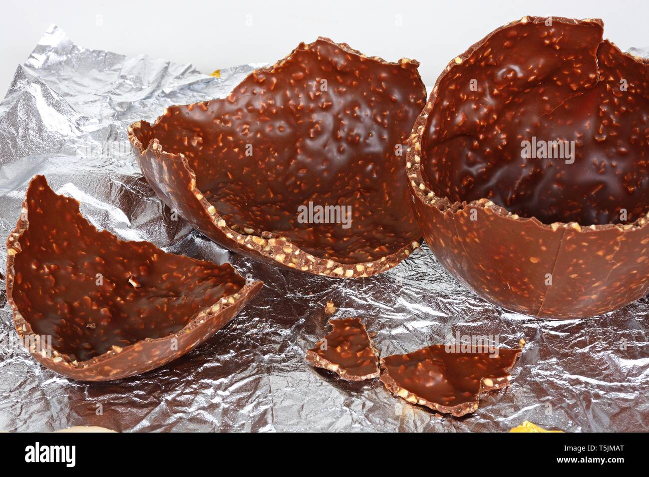 Broken chocolate Easter egg with chopped hazelnuts on a foil sheet against, UK. Stock Photo