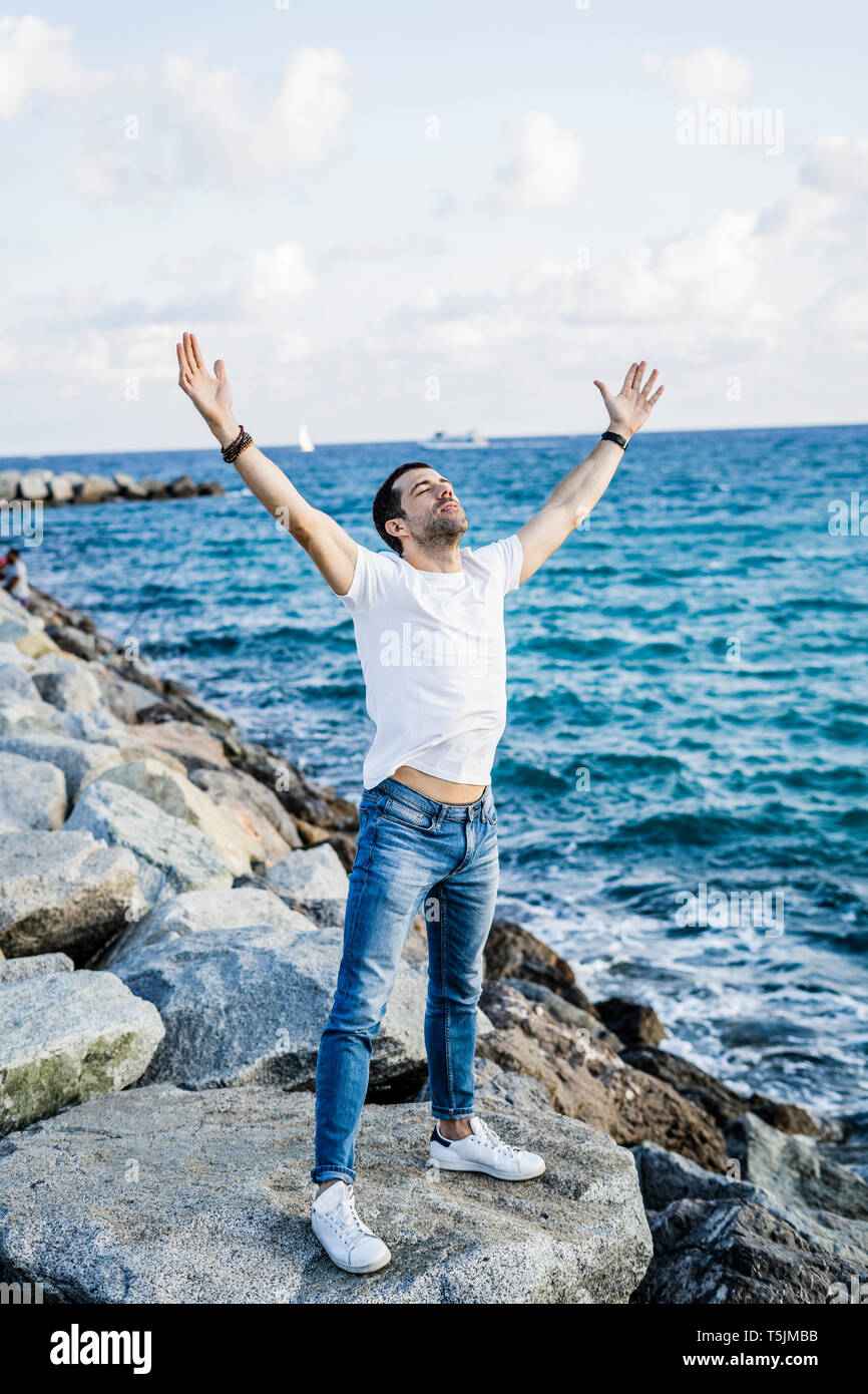 Man with raised arms and eyes closed standing in front of the sea Stock Photo