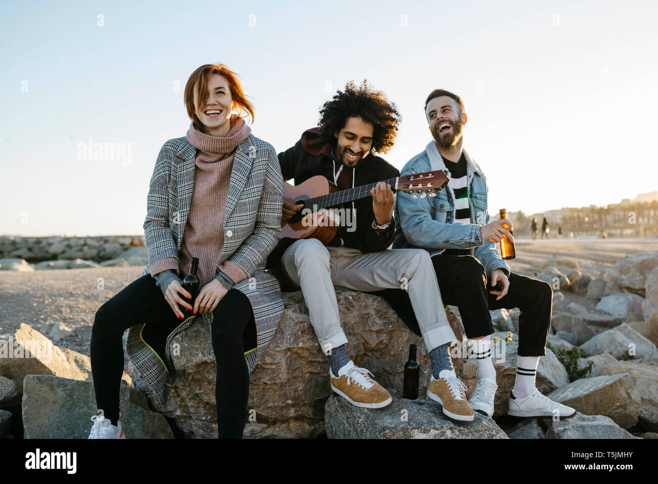 Three happy friends with guitar sitting outdoors at sunset Stock Photo