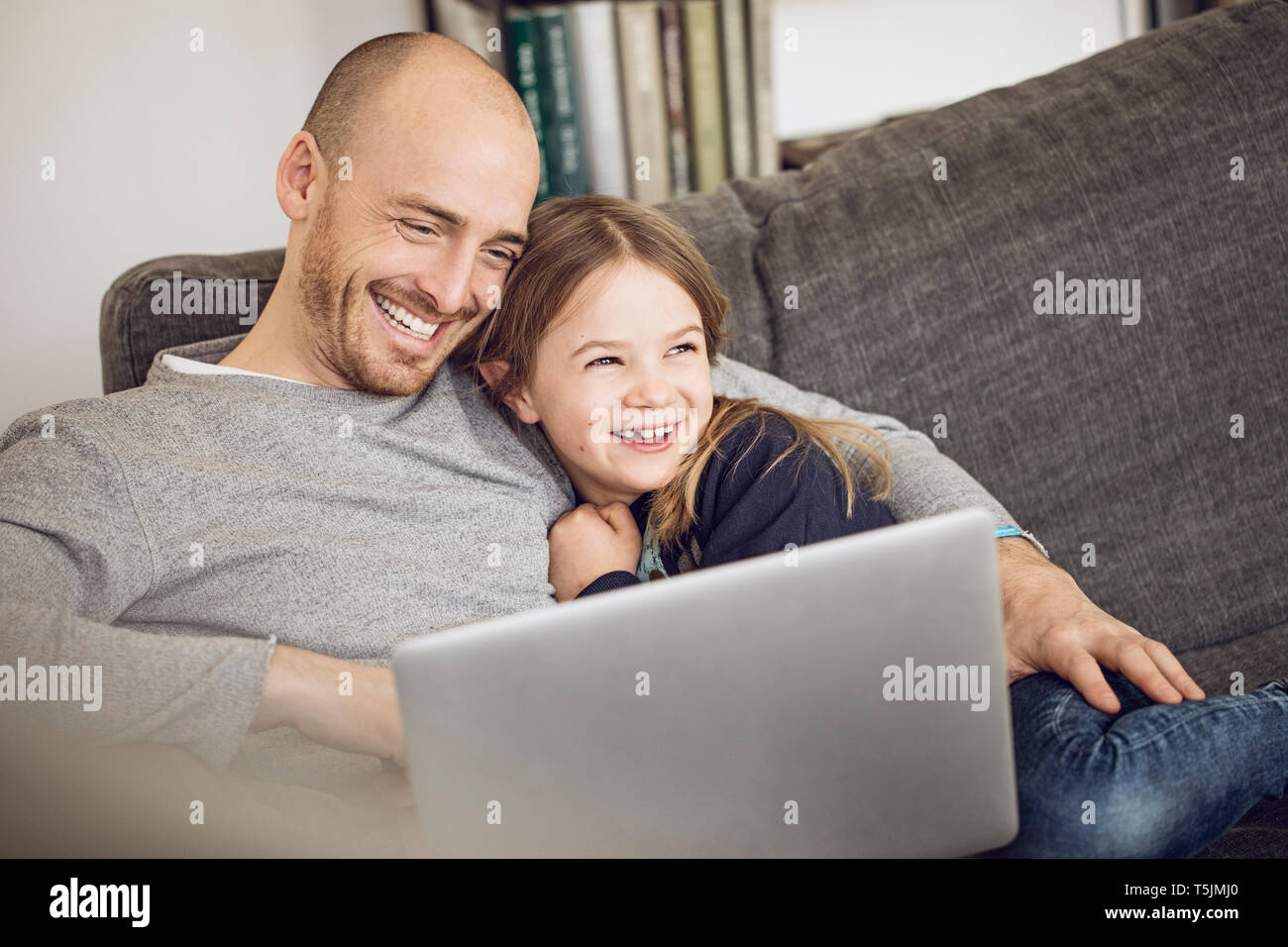 Father and daughter sitting on couch, using laptop Stock Photo