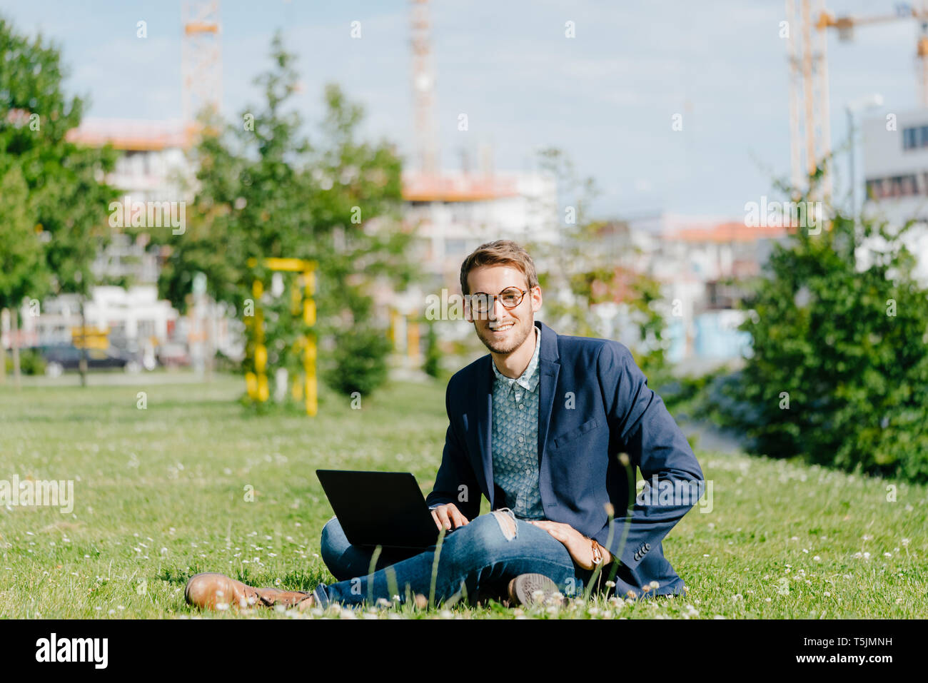 Young businessman sitting in park, using laptop Stock Photo