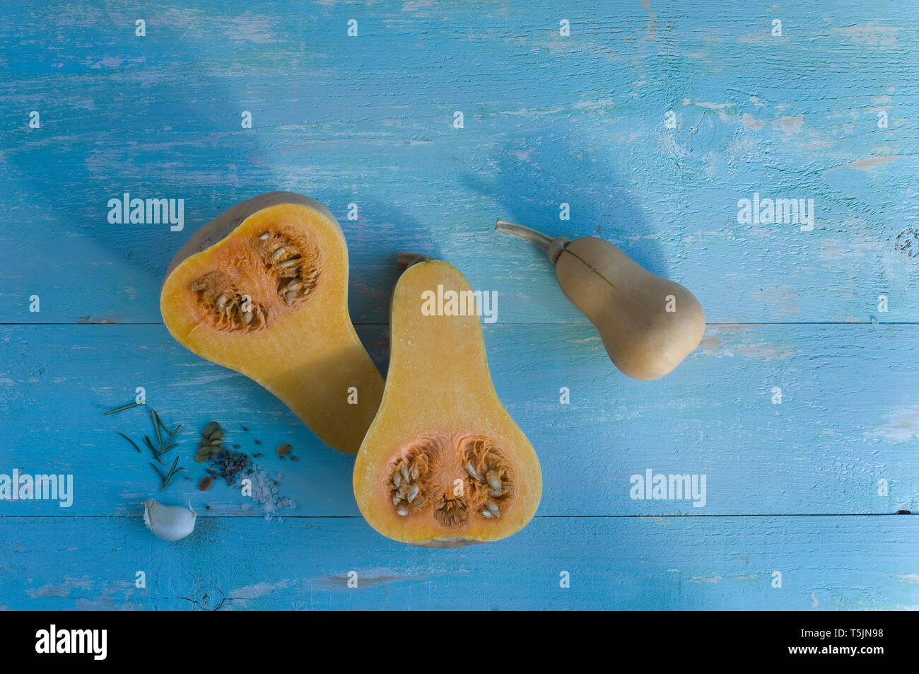 Whole and sliced butternut squash, garlic clove and herbs on light blue wood Stock Photo
