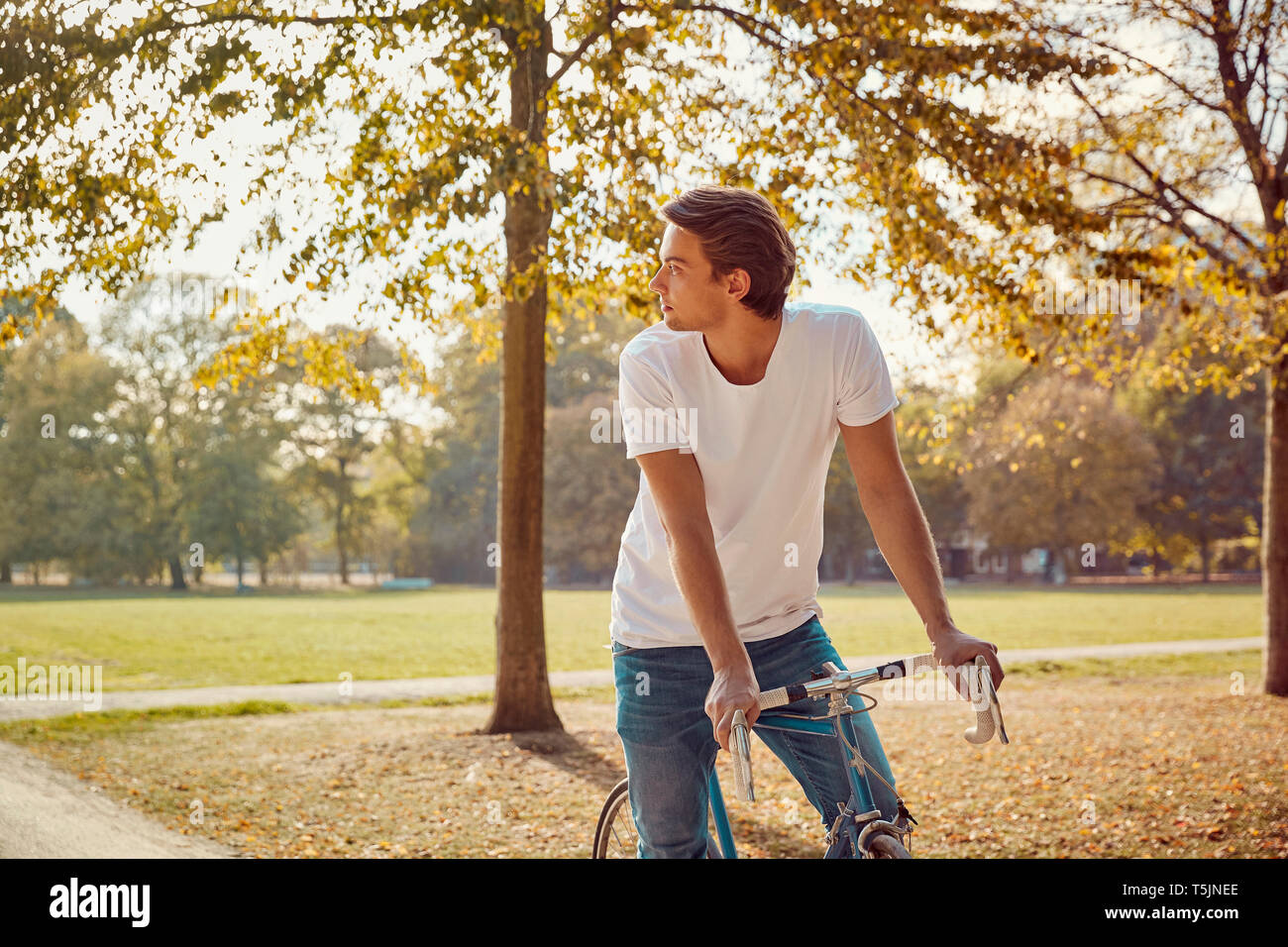 Young man with bike in park looking around Stock Photo