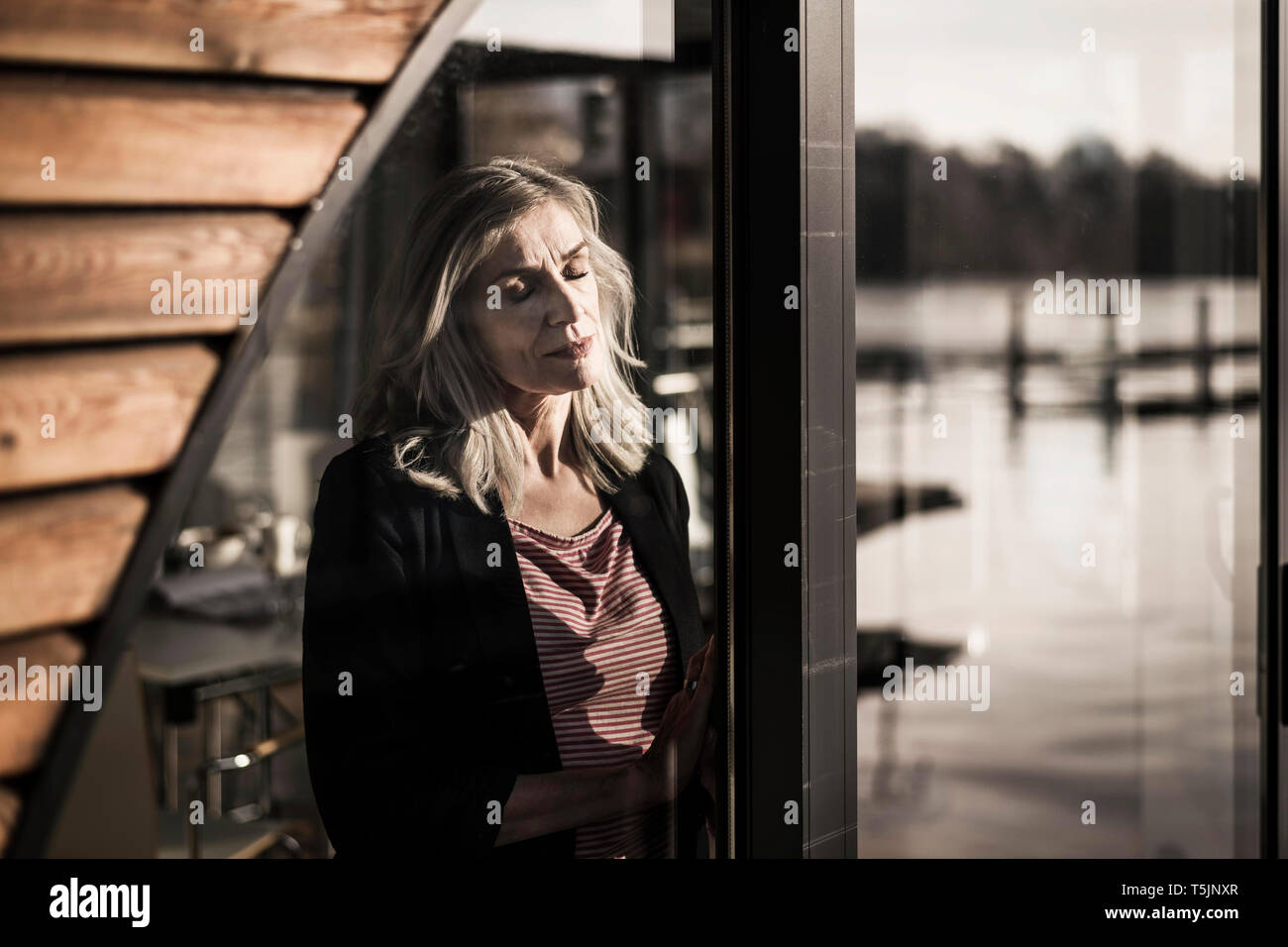 Businesswoman standing on a houseboat,enjoying the sun at the window with eyes closed Stock Photo