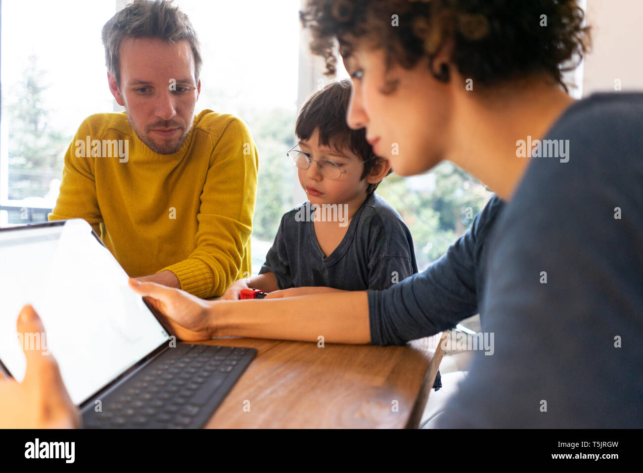 Family sitting at table, using digital tablet Stock Photo