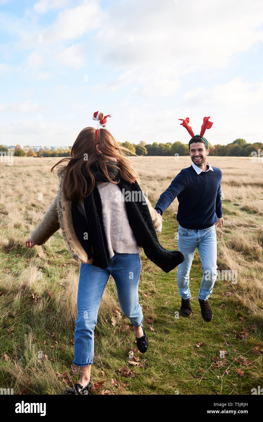 Happy carefree couple wearing Christmassy headdress running in the countryside Stock Photo