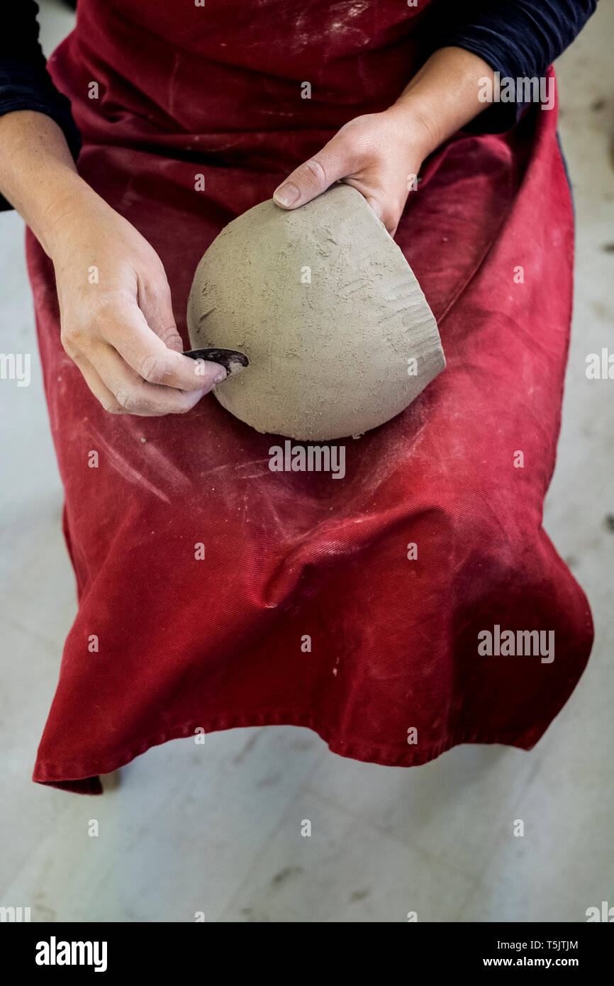 High angle close up of ceramic artist wearing red apron sitting in her ...