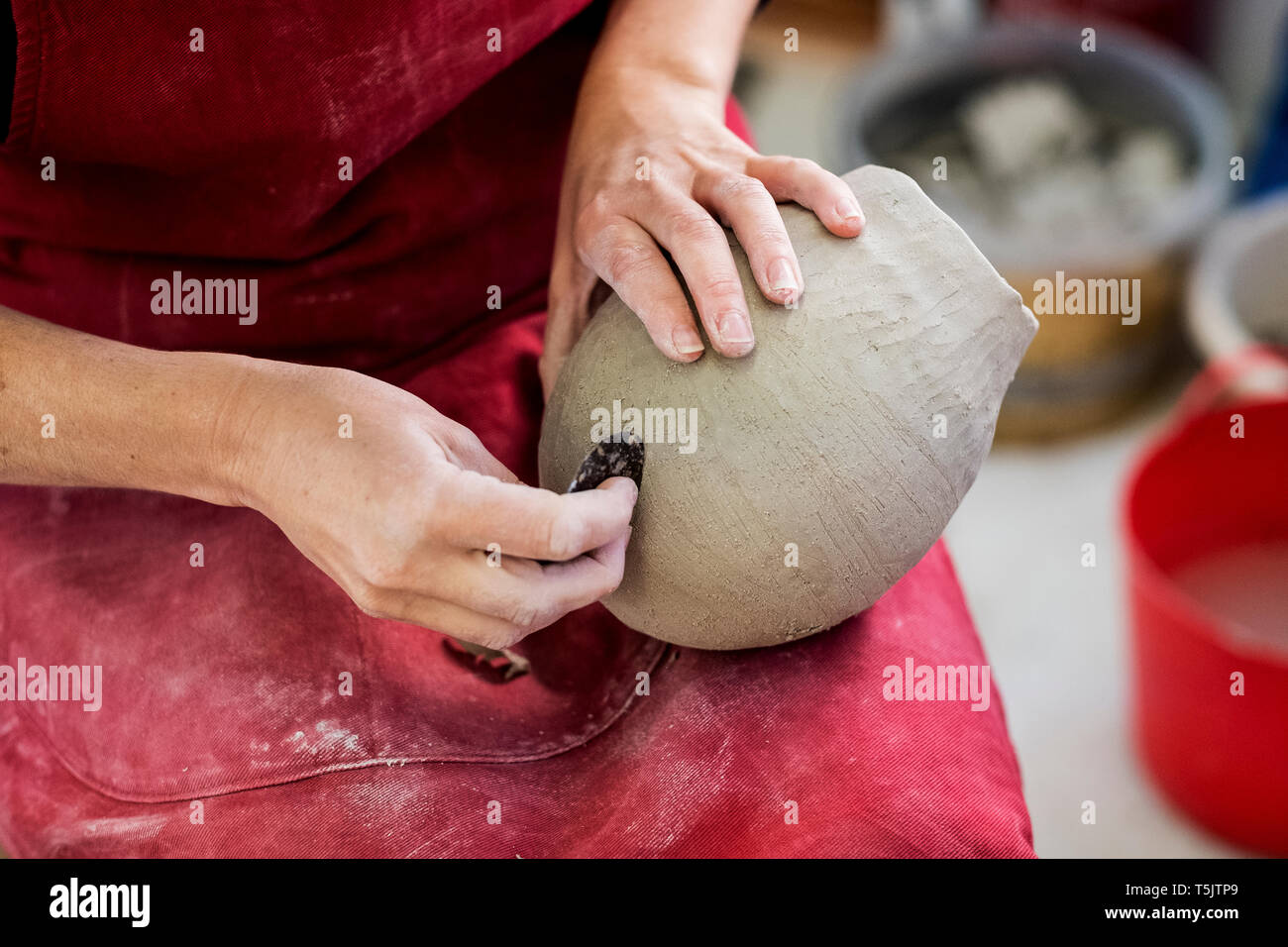 High angle close up of ceramic artist wearing red apron sitting in her ...