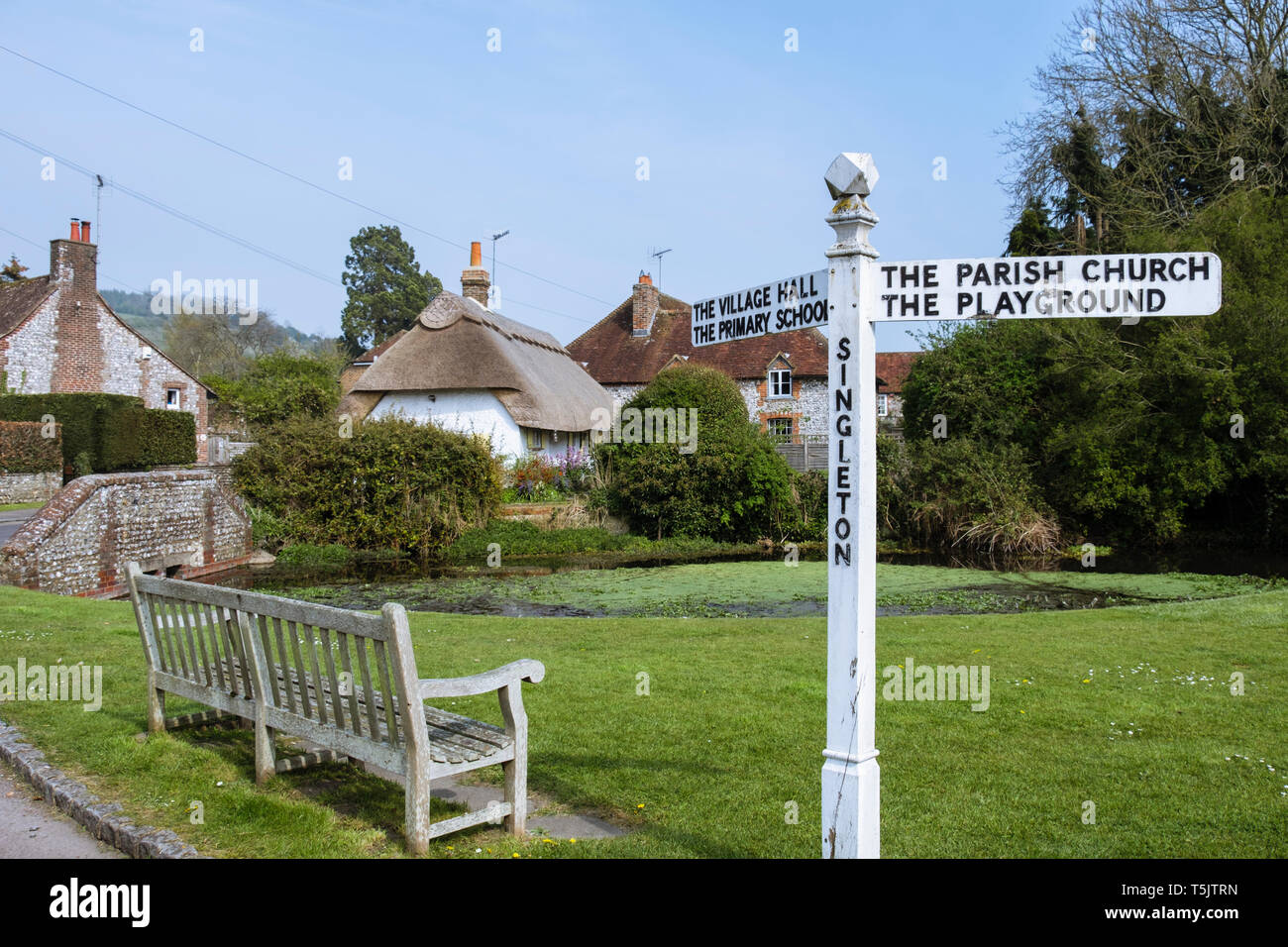 Empty bench and signpost on a country village green by pond in South