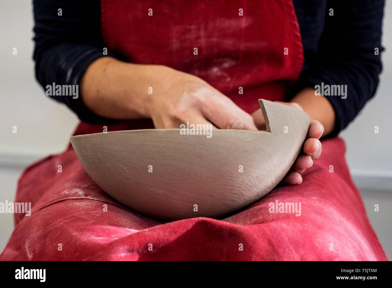 Close up of ceramic artist wearing red apron working on clay bowl. Stock Photo
